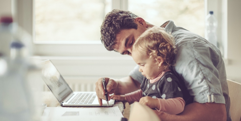 A father engaging his child while working at home, sitting at his computer