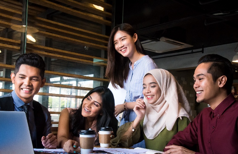 A group of five people smiling while looking at a computer screen