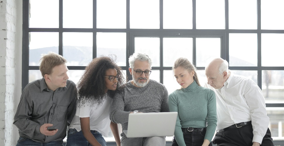 A group of workers of different age groups looking at one laptop screen