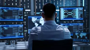 Person working at a desk with multiple computer monitors displaying data and maps.