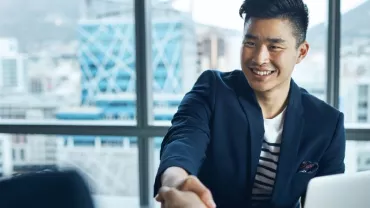 Two people shaking hands in an office with city view in background.