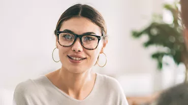 Woman with glasses and hoop earrings talking to two people.