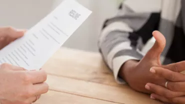 Interview scene with two people at a table, one holding a resume.