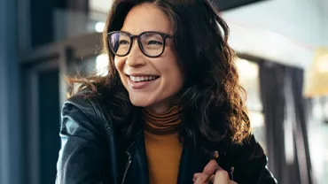 Person in glasses smiling indoors, wearing a leather jacket.