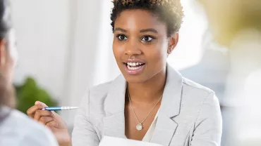 Woman in a gray suit holding a pen, engaged in conversation.