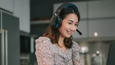 Smiling woman in headphones working on a laptop in a modern kitchen.