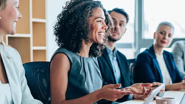 A diverse group of people smiling and talking in a meeting room.