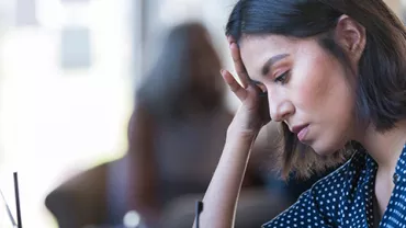 Woman in polka dot shirt looking thoughtful while working at a desk.