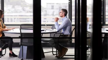 Two people having a meeting in a glass-walled office.