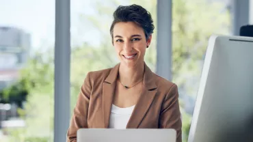 Smiling woman at her desk with a computer in a modern office.