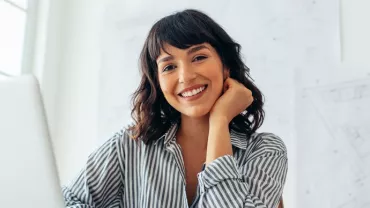 Smiling person in a striped shirt at a desk with architectural plans.