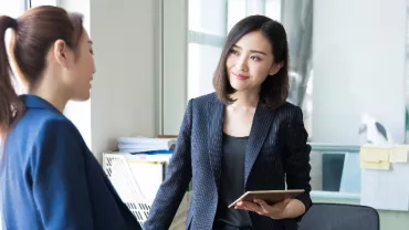 Two women in business attire having a conversation in an office.