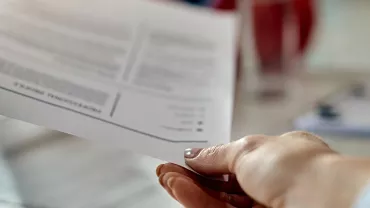 Close-up of a person's hand holding a document over a table.