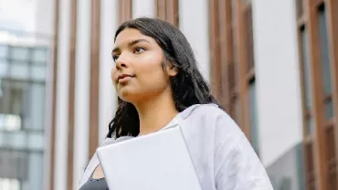 Young woman with a laptop, standing outside a modern building.