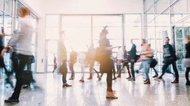 Blurred motion of people walking through a busy glass entrance.