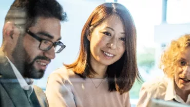 Three people in a meeting, smiling and discussing around a laptop.