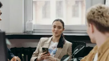 Three people having a discussion in a modern office with plants.