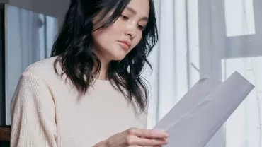 Woman in a white sweater reading a document while sitting indoors.