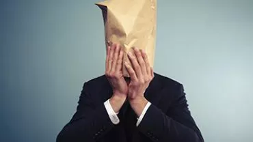 Person in a suit with a paper bag over their head, against a plain background.