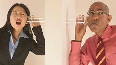 Two people using cups to listen through a wall.