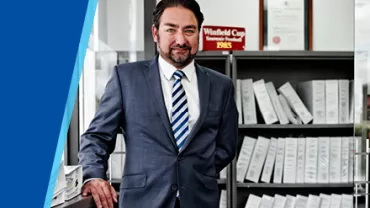 Man in a suit standing in an office with shelves of binders.