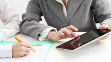 Two business people working on documents and using a tablet.