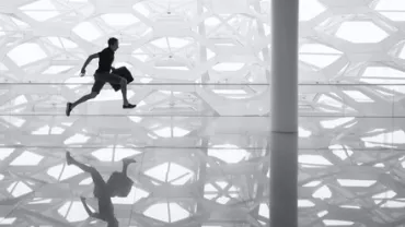 Silhouette of a man running indoors with a patterned wall reflection on the shiny floor.