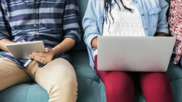 Two people sitting on a sofa with a tablet and a laptop.