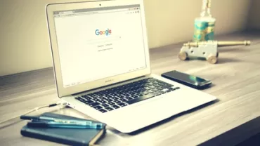 Laptop with Google search on screen, placed on a desk with a phone and notebook.