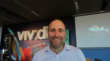 Smiling person in front of Vivid Sydney poster with colorful design elements.