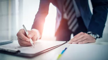 Businessperson in a suit writing in a notebook at a desk.