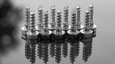 Nine shiny metal screws standing upright on a reflective surface.