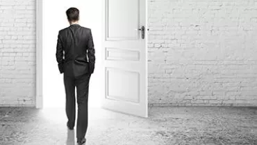 Man in a suit walking through an open door into a bright space.