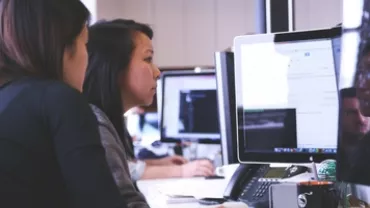 Two women collaborating at a computer in an office setting.