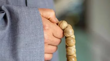 Person in gray robe holding wooden prayer beads.