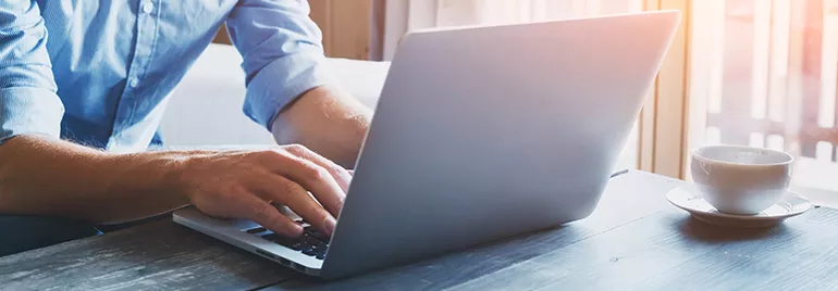 Person typing on a laptop at a wooden table with a cup of coffee.