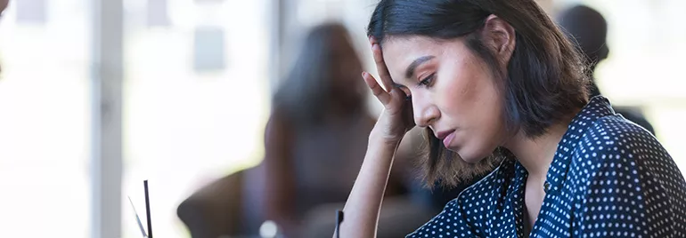 Woman in polka dot shirt looking thoughtful while working at a desk.