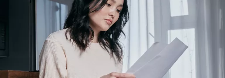 Woman in a white sweater reading a document while sitting indoors.