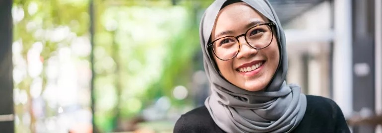 Woman in glasses and hijab smiling in an indoor setting.