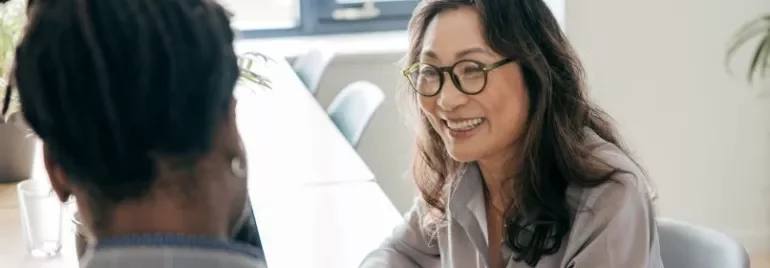 A woman in glasses converses with a man in an office setting, both engaged in discussion.