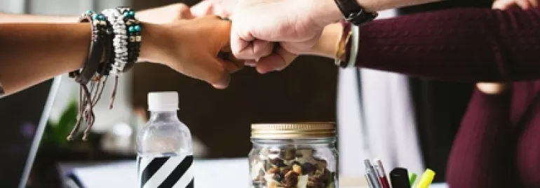 Four people fist bumping over a table with office supplies.