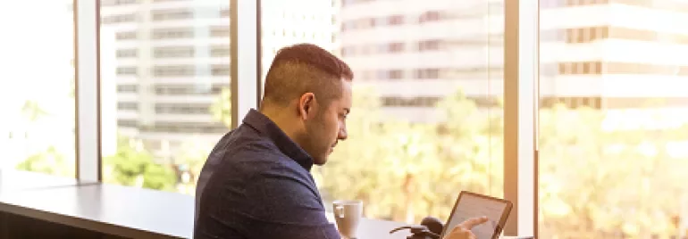 Man working on a tablet by a window with city view.