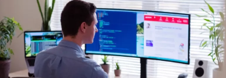 Person working at a desk with two computer screens displaying code and a website.